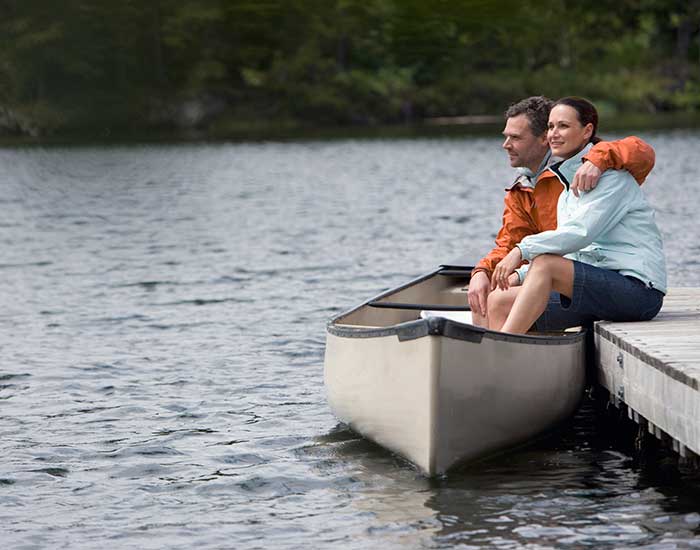 Couple sitting on pier with legs in canoe, looking at view